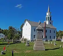A white church, seen from the side slightly to its rear, with a cemetery in front