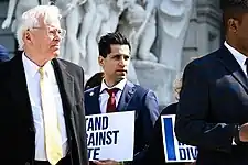 Khan stands with a poster reading "Stand Against Hate"