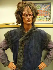 An orange mannequin wearing a wig and heavy prosthetic make-up on its face.