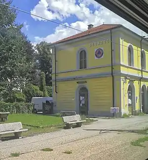 Two-story building with gabled roof next to railway tracks, viewed from a moving train