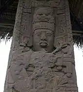 Close up of upper portion of an intricately carved stela, showing the face of a king with elaborate headdress and jewellery