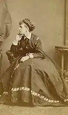 Boulton sitting in profile, wearing an Edwardian dress, with an elaborate wig