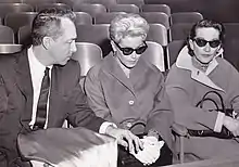 Two women wearing sunglasses seated next to a man
