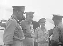 Four men in uniform with peaked caps talking to each other.