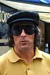 Jackie Stewart wearing a yellow T-shirt, a black cap and sunglasses