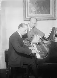 Black and White photo of Stravinsky playing an upright piano, Furtwangler sitting beside him studying the score