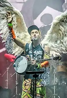 Stevens onstage with his eyes closed and hand raised in front of a microphone with a banjo slung around his shoulder and wings on his back