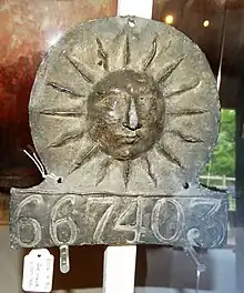 A metal plaque with a sun in the middle and numbers 667403