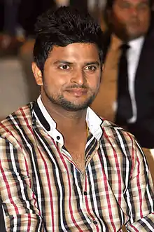 An Indian cricketer wearing a multi-colored shirt. Others can be seen in the background.