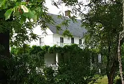 Photograph of a two-story house partially obscured by vegetation