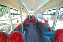 View down the saloon of Lynx's T29 KLN, refurbed R17 TYB, showing an ashy woodgrain flooring under seats upholstered in fiery moquette suspended from gleaming white saloon walls behind sweeping partitions with bright white LED uplighting above