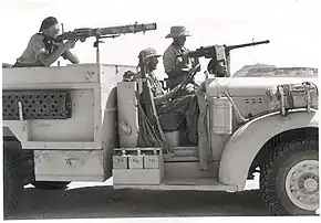 posed picture of three men one sitting in the drivers seat and the other two aiming machine guns