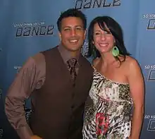 A strong Filipino man in a brown suit poses for a picture with his Italian wife who is wearing a colorful zebra print dress.