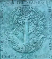 Copper plaque with patina depicting two foxes under a tree. Around the outside is the inscription: "Under the seat beside the water makes a home for a' Jock Tamson's bairns"