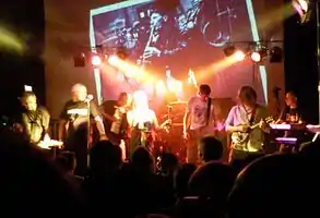 The Tansads on stage at one of their 2010 reunion gigs.  Visible from left to right: John Kettle, Andrew Kettle, Dominic Lowe, Janet Anderton, Phill Knight, Ed Jones, Bob Kettle, Lee Goulding