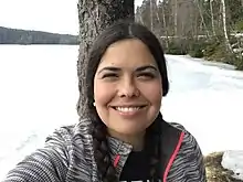 Tara Houska smiling and looking directly at the camera, standing in snow covered woods