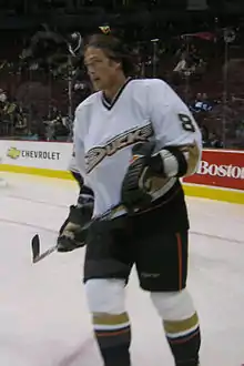 A brown haired hockey player in a white and black uniform with the wordmark "Ducks" across his chest skates as he looks into the distance.