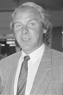 A photograph of a man with blond hair wearing a suit.