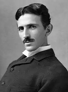 Head-and-shoulder photograph of a slender man with dark hair and moustache, dark suit and white-collar shirt
