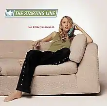 A woman sitting on the end of a sofa, talking into a telephone