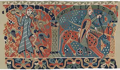 Vividly colored woven tapestry fragment depicts two men. On the left, a standing man is surrounded by birds. On the right, an armored man rides a horse.