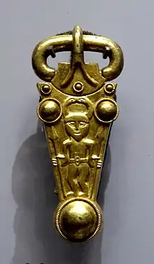 A gold buckle decorated with a man in a horned helmet carrying a spear in each hand.