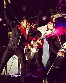 Three band members singing, wearing red and black uniforms.