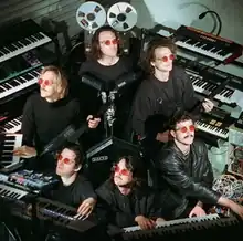 The band standing together, surrounded by keyboards