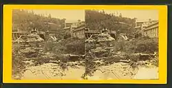 Old black and white photo of a waterfall, flanked on both sides with slightly dilapidated-looking buildings.