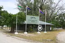 An exterior photo of the current South Pacific WWII Museum's 'mini museum' which is located in Unity Park in Luganville, Espiritu Santo, Vanuatu. Flag poles fly the Vanuatu, Australian, New Zealand and USA plags.