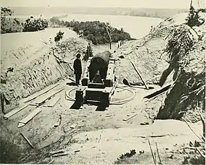 Black-and-white photo of a cannon overlooking a river curve