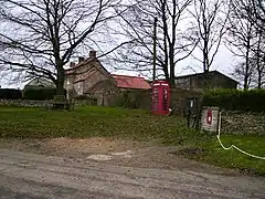 A red post-box and a red telephone box, with trees and a small collection of buildings beyond