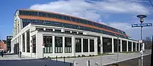  A long, large building with a barrel-vault roof rising above a facade with full-length plate-glass windows along the length of the building