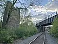 THREE RAILROADS CROSS AT A RIVER: Stretching from the center to the right are the still-active rails of the Providence and Worcester Railroad. The bridge above and to the right carried what was once the Southbridge and Blackstone Railroad; today it carries the Blackstone River Greenway. On the left is a bridge support for the never-completed Southern New England Railway; had the bridge been constructed, it would have crossed high above the other two lines, from near left to near right. All three alignments cross the Blackstone River within yards of each other, at this point in Millville, Massachusetts known as Triad Bridge.