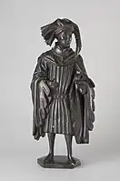 Figure E: Man wearing a chaperon (an elaborate hood popular in the mid-15th century). He has an elaborately ornamented belt, and his sleeves are unusually wide and flare at their ends. The cross around his neck reflects the Order of St. Anthony.