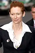 Tilda Swinton with slicked-back hair wearing suit and looking to the left
