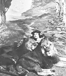 Portrait of a woman seated on the ground holding three lions in her lap in front of a backdrop of trees and mountains.