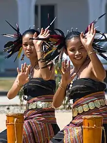 Two women dancing in traditional outfits incorporating feathers and tais cloth
