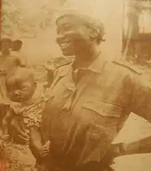Photograph of Titina Silá, holding one of her children, while dressed in her militia uniform