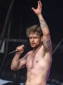 A topless man with a microphone appears on stage
