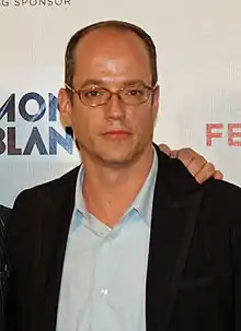 Tom Kalinwearing glasses and a vest outside a light blue shirt, looking to the front