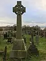 On the left stands a large tombstone erected for James Campbell in the style of a Celtic cross. On the right stands a much smaller regular cross which is the tombstone of his wife Jane.