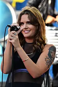 A woman wearing a white top and a silver skirt holding a microphone near her mouth
