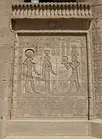 Relief on a screen wall between columns at Dendera, with images of marsh plants at the base, torus moldings framing the relief, and a cavetto cornice with a winged sun emblem topped by a frieze of uraei. First to second century AD.