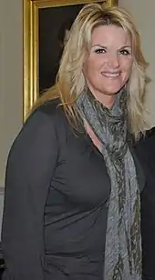 A woman with long blonde hair wearing a grey top and a grey scarf
