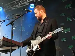 Man playing keyboard while holding a guitar