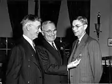 three men in suits. The one on the right is wearing a medal.