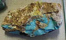 An uncut nodule of brown matrix with a split face showing areas of turquoise.