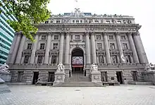 A low-front image of the Alexander Hamilton U.S. Customs House. In front of the building is a short staircase with statues stood on either side. There are several windows covering the front of the building.