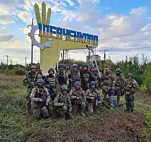 Soldiers of the Territorial Defence Forces of Ukraine near the freshly repainted (from Russian flag colors into Ukrainian ones) entrance mark in Shevchenkove, liberated after the Kharkiv counteroffensive